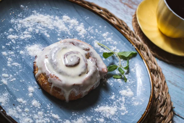 Mavi tabakta ev yapımı Cinnabon Bun ve çayla birlikte sarı bardak. Seçici odak