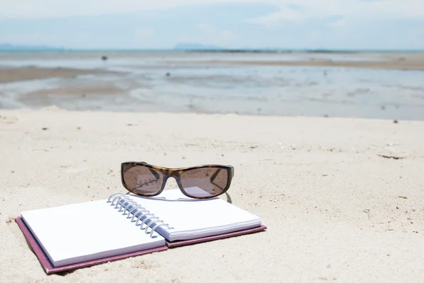 Notebook en sunglass op strand — Stockfoto