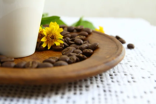 Grãos de café e xícara branca com flor de margarida em prato de madeira — Fotografia de Stock