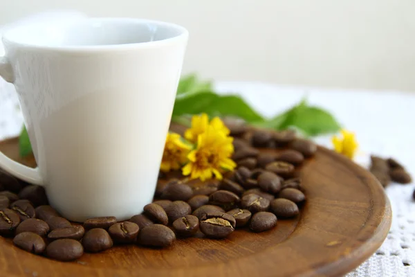 Grãos de café e xícara branca com flor de margarida em prato de madeira — Fotografia de Stock