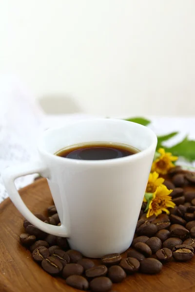 Grãos de café e xícara branca com flor de margarida em prato de madeira — Fotografia de Stock