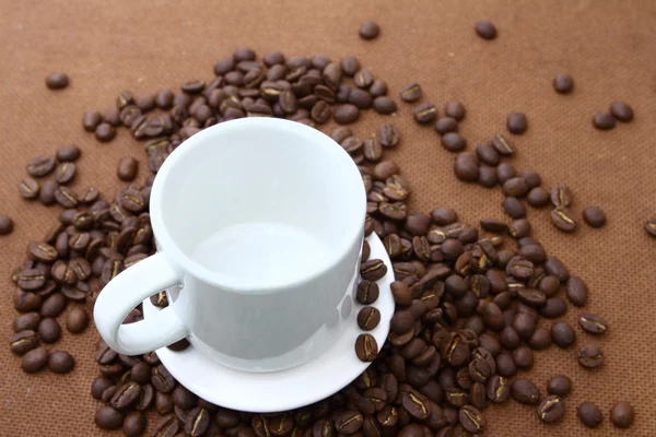 Kávová zrna a bílý šálek na dřevěné desce — Stock fotografie