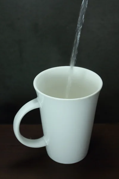 Vierta el agua en una taza de cerámica sobre una mesa de madera — Foto de Stock