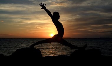 mükemmel vücut insan silüeti yoga deniz sunet geçmişi olan kaya üzerinde hareket eder.