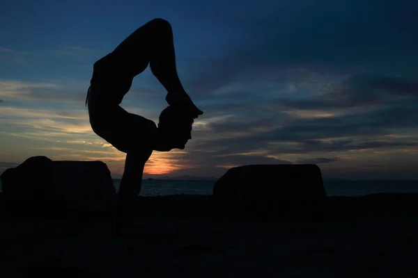 Silhouette of perfect body man acts yoga on the rock with sea sunet background — Stock Photo, Image