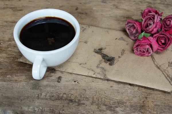 Vieux papier roses roses et tasse à café noire sur table en bois grunge — Photo