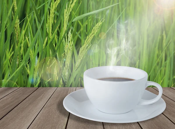Šálek kávy na dřevěnou podlahu, s neloupanou rýži pole pozadí — Stock fotografie