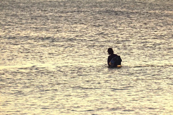 Silhouette of young fisherman in ocean at sunset — Stock Photo, Image