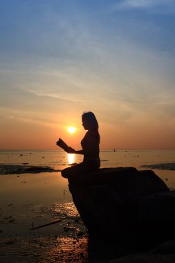 gün batımında sahilde kayada siluet kız okuma kitabı