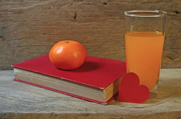 Fruta de mandarinas de miel, jugo con papel en forma de corazón y libro antiguo sobre mesa de madera —  Fotos de Stock