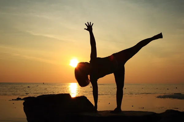 Silhouette yoga girl by the beach at sunrise doing Half Moon Pose — Stock Photo, Image