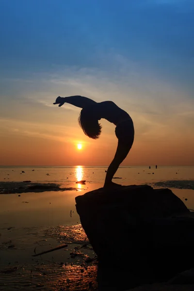 Silueta yoga chica haciendo la rueda pose en roca por playa puesta de sol — Foto de Stock