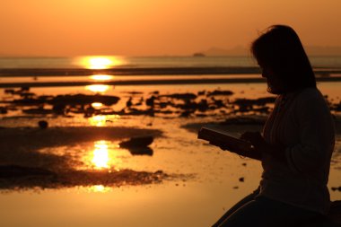 siluet kadın doğarken sahilde kitap okuma