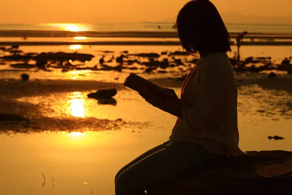 日出时分，海滩读书的剪影女人 — 图库照片