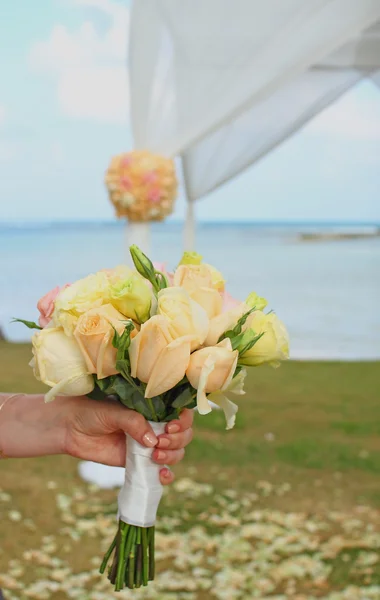 Hand hold the bride's bouquet consists of roses with seascape background — Stock Photo, Image