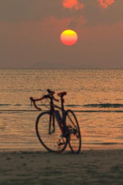 Silhueta de uma bicicleta na praia ao pôr-do-sol vermelho fundo — Fotografia de Stock