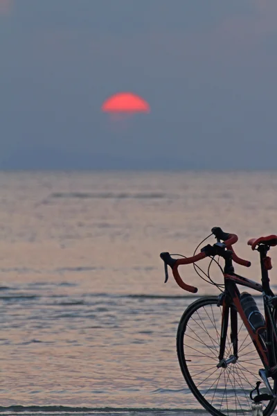 Silhouette egy kerékpáros, a strandon található vörös naplemente háttér — Stock Fotó