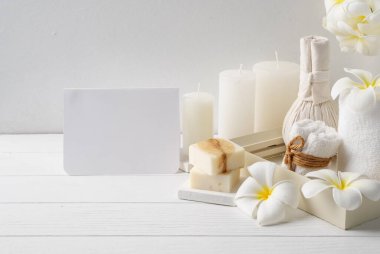 Masaj kulaklı spa davetiyesi vazoda bir çiçek hindistan cevizi kahve sabunu, beyaz havlular ve beyaz ahşap masa zemininde mum, yumuşak beyaz tonu natürmort hayat.