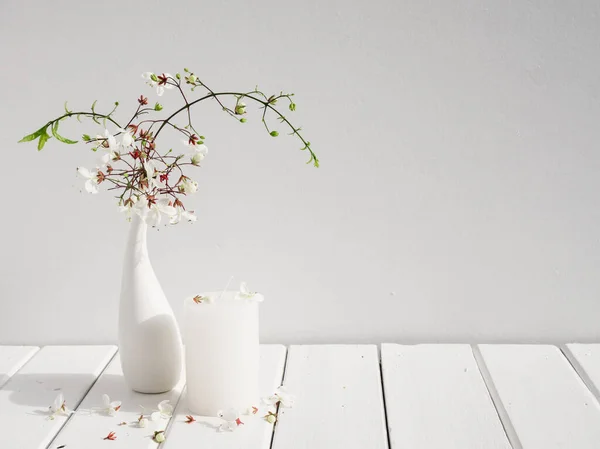 白い木製のテーブルルームのインテリア 夏の柔らかいトーンの静物画の上に現代的なガラス花瓶組成の白いキャンドルと美しいうなずきクレロデンダーの花 — ストック写真