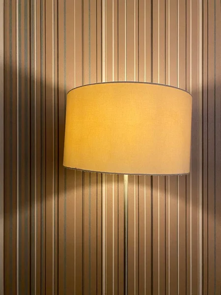 Classic yellow lamp with lampshade against a striped wall