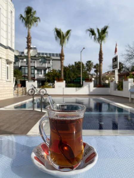 Hot turkish tea outdoors near water. Turkish tea and traditional turkish culture concept. Vertical. Turkish glass for tea on the background of the pool.