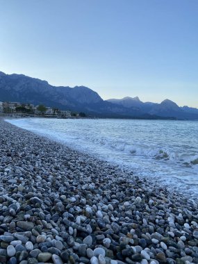 Deniz kıyısında çakıl taşları, deniz arka planı. Bir deniz dalgası sabahın erken saatlerinde çakıl taşı plajını yıkar. Yakın plan. Kemer, Türkiye