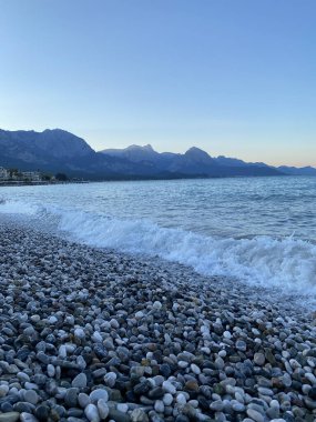 Deniz kıyısında çakıl taşları, deniz arka planı. Bir deniz dalgası sabahın erken saatlerinde çakıl taşı plajını yıkar. Yakın plan. Kemer, Türkiye