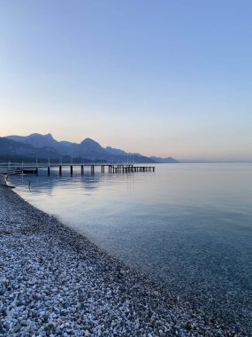 Deniz kıyısında çakıl taşları, deniz arka planı. Bir deniz dalgası sabahın erken saatlerinde çakıl taşı plajını yıkar. Yakın plan. Kemer, Türkiye