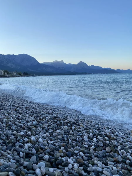Deniz kıyısında çakıl taşları, deniz arka planı. Bir deniz dalgası sabahın erken saatlerinde çakıl taşı plajını yıkar. Yakın plan. Kemer, Türkiye