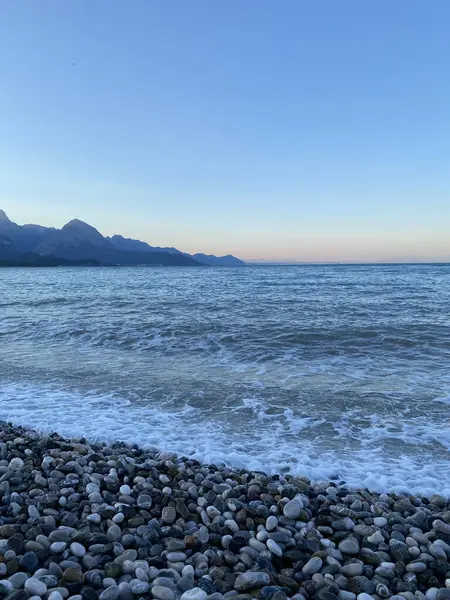 Deniz kıyısında çakıl taşları, deniz arka planı. Bir deniz dalgası sabahın erken saatlerinde çakıl taşı plajını yıkar. Yakın plan. Kemer, Türkiye