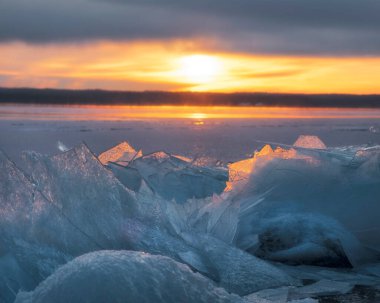 Güneş, gün batımında, buz gibi kışlarla kaplı bir orman gölünün kıyısında parlar..