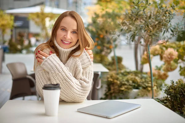 Tıknaz örgü kazaklı kadın kahve içer ve şehir kafesinde ısınır. sıcak gölgeler yatay fotoğraf