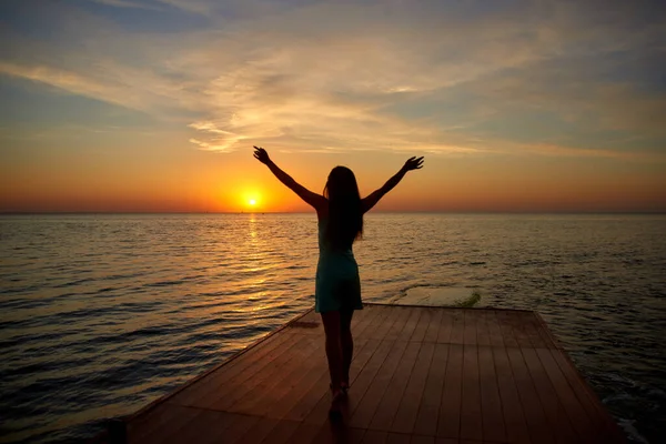 海边的日出或黎明 站在码头上的侧影女孩举手表决太阳 浅水区深度 — 图库照片