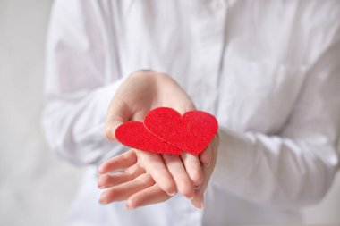 Beyaz gömleğin arka planında iki kalp tutan bir kadın. Alan fotoğrafının yüzeysel derinliği