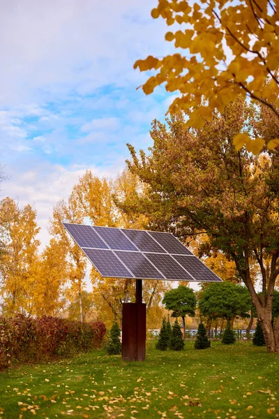 Environmental protection solar panels in city park on sunny fall day. Beautiful yellow trees in autumn
