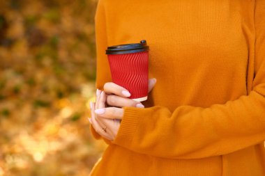 morning take away coffee. paper cup advertisement. coffee to go in woman hands on fall yellow background. shallow depth of field