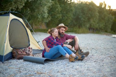 resting couple of woman and man sit near tent in camping, hugs, spend time together in weekend