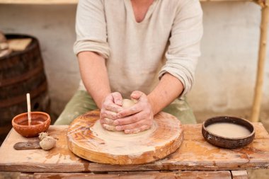 Potter male master in light linen shirt with wet clay pot in hands. pottery hobby man hands sculpt in clay