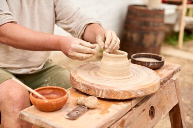 male craftsman master in light linen shirt sculpts jug, bowl or vase from clay in country