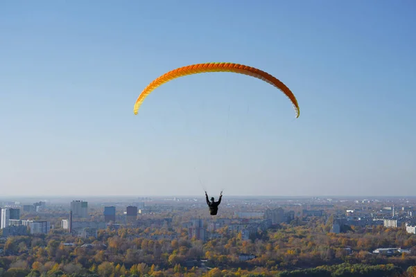 Bir paraglider şehrin arka planında, evlerde ve mavi gökyüzünde güneşli bir havada planör uçurur..