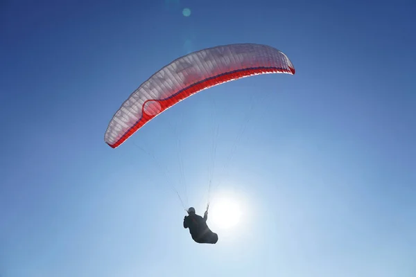 Bir paraglider, güneşli bir havada mavi gökyüzüne karşı planör uçurur. Kapat..