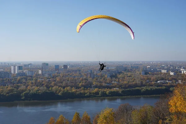 Bir paraglider şehrin arka planında, evlerde ve mavi gökyüzünde güneşli bir havada planör uçurur..