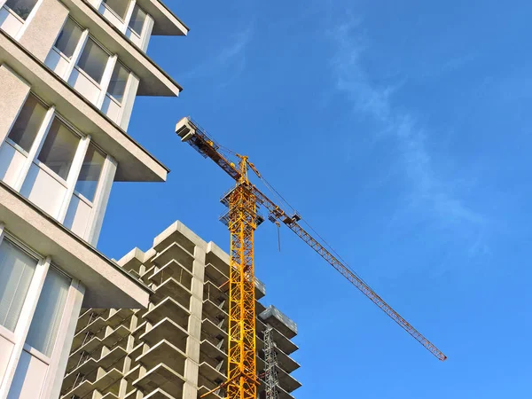 Mavi arka planda sarı bir vinci olan çok katlı bir binanın yapımı.