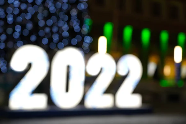 The inscription of the numbers 2022 on the background of a Christmas tree with blue lights and garlands