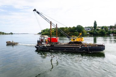 Kappeln, Almanya - 07 Eylül 2021: Endüstriyel vinçle bir mavnayı su yüzeyinde çeken bir römorkör