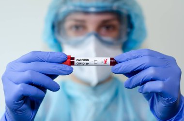 Tıbbi laboratuvar asistanı Omicron COVID-19 kan örneğiyle test tüpü tutuyor..