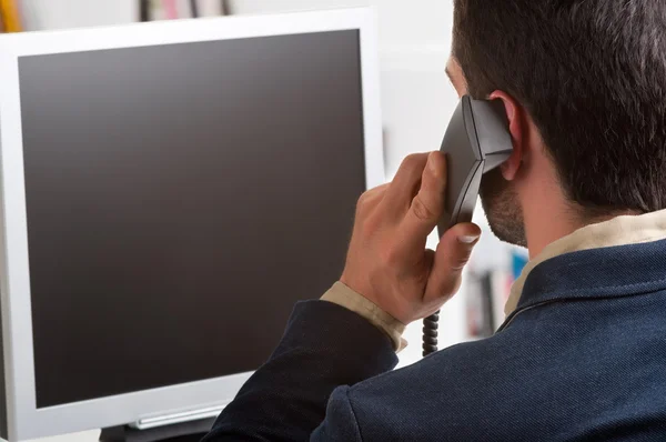 Empresario casual hablando por teléfono y mirando a una compu — Foto de Stock
