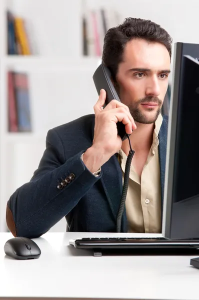 Mann schaut auf Computermonitor, am Telefon — Stockfoto