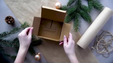 Kadınların elleri Noel ve yeni yıl hediyelerini çevre dostu malzemelerle paketliyor: el işi kağıt, canlı köknar dalları, koniler, sicim, yayla bağlanmış. Doğal dekor, el yapımı, düz. Şenlik havası