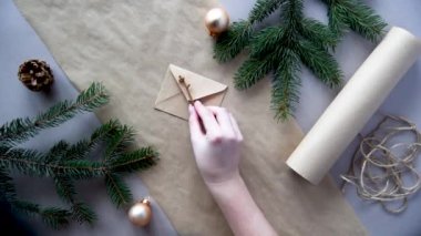 Kadınların elleri Noel ve yeni yıl hediyelerini çevre dostu malzemelerle paketliyor: el işi kağıt, canlı köknar dalları, koniler, sicim, yayla bağlanmış. Doğal dekor, el yapımı, düz. Şenlik havası